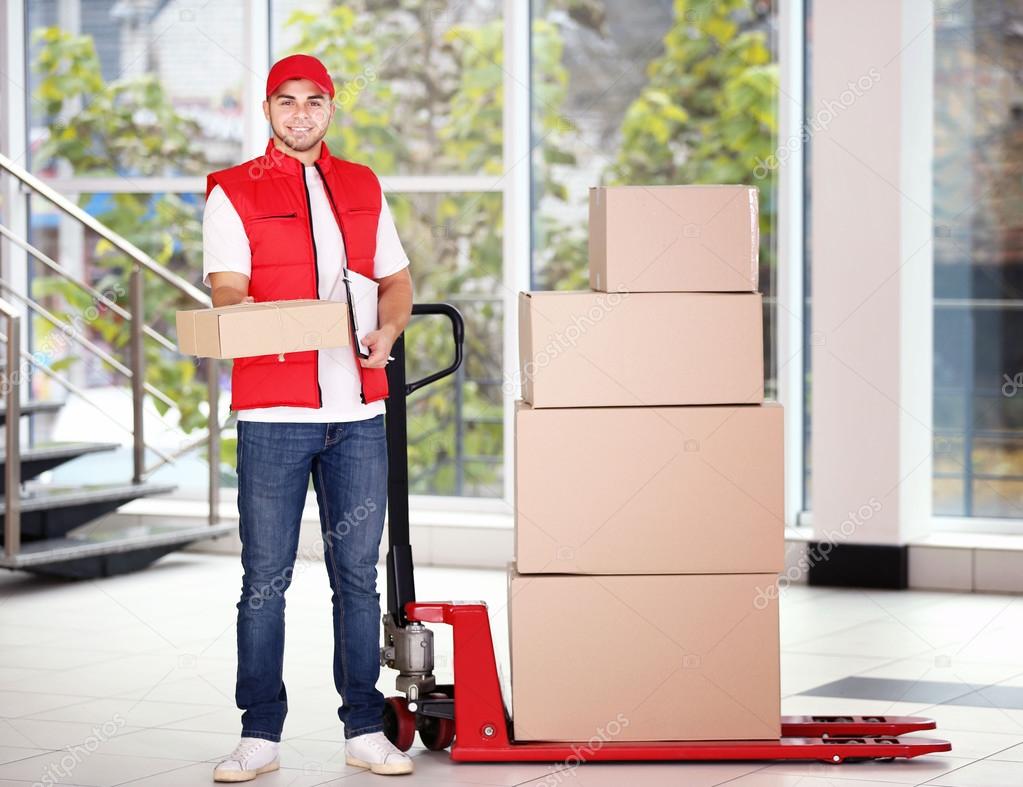 Postman in red uniform with parcels on dolly