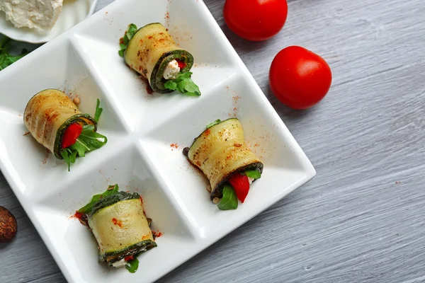 Rollos de calabacín con queso, pimientos y rúcula en el plato, primer plano, sobre fondo de mesa — Foto de Stock