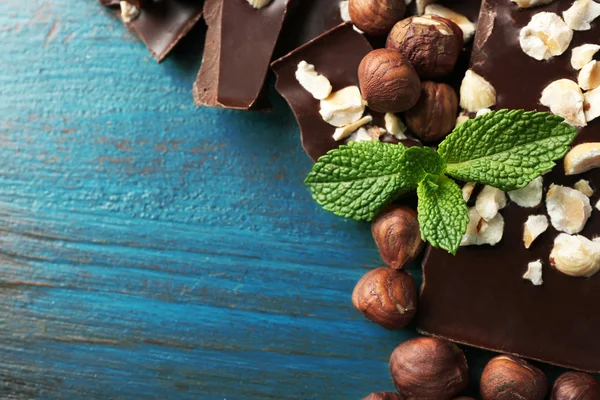 Pezzi di cioccolato con noci su sfondo di legno colore — Foto Stock