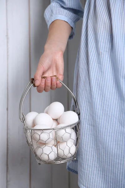 Jajka w koszyku kobiet w ręce na drewniane tła — Zdjęcie stockowe
