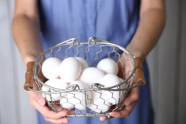 Ovos na cesta em mulheres mãos no fundo de madeira — Fotografia de Stock