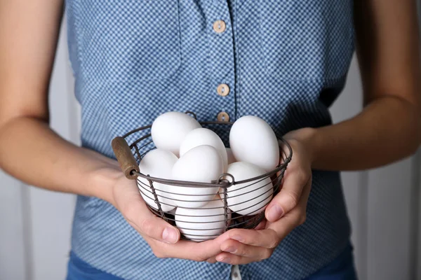 Huevos en cesta en las manos de las mujeres sobre fondo de madera —  Fotos de Stock