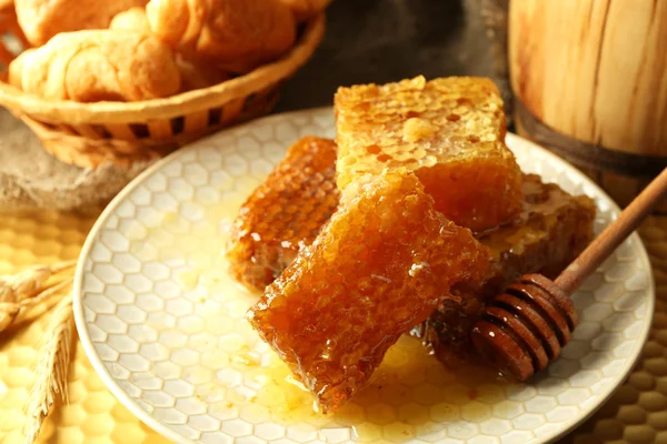Pentes de mel na placa, pães quentes na cesta no fundo de madeira — Fotografia de Stock