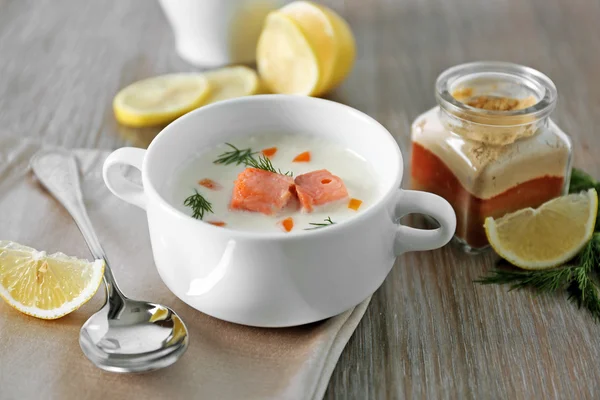 Вкусный кремовый суп из лосося на деревянном столе, который подается с нарезанным лимоном и специями — стоковое фото
