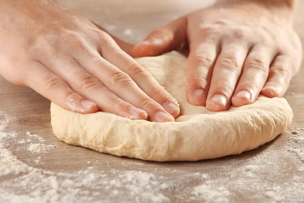 Mãos amassando massa para pizza na mesa de madeira, close-up — Fotografia de Stock