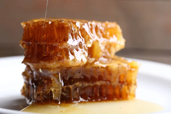 Miele gocciolante su favi su piatto su fondo di legno — Foto Stock