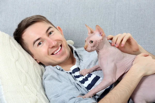 Pohledný muž leží s kočkou na gauči — Stock fotografie