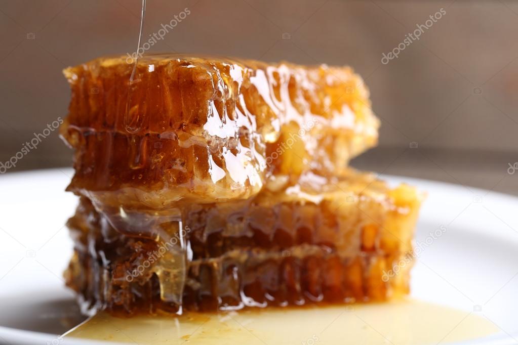 Honey dripping on honeycombs on plate on wooden background