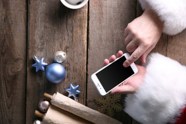 Noel kavramı. Akıllı telefon ahşap masa üzerinde eller Santa alır yakın çekim
