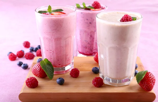 Молочные коктейли при разрезании доски с ягодами на светлом фоне — стоковое фото