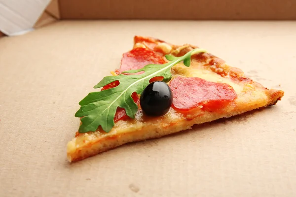 Plak van pepperoni pizza met rucola en olijven op karton — Stockfoto