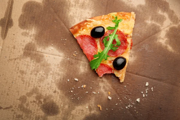 Fetta di pizza al salame piccante morsa con olive e rucola su cartone — Foto Stock
