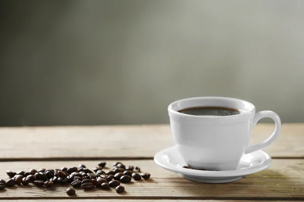 Secangkir kopi dan biji-bijian kopi di atas meja kayu, dengan latar belakang abu-abu — Stok Foto