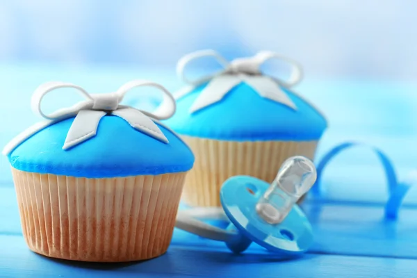 Tasty cupcake with bow and baby shoes on color wooden background — Stock Photo, Image