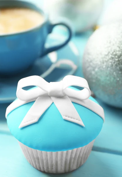 Leckerer Cupcake mit Schleife, Kaffeetasse und Weihnachtsspielzeug auf farbigem Holzhintergrund — Stockfoto