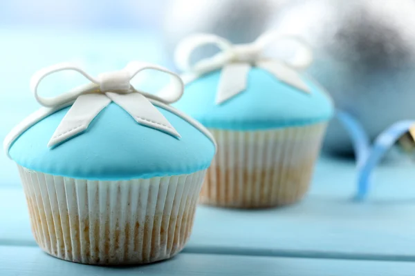 Tasty cupcakes with bow and Christmas toys on color wooden background — Stock Photo, Image