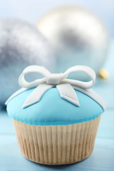 Cupcake saboroso com arco e brinquedos de Natal na cor de fundo de madeira — Fotografia de Stock