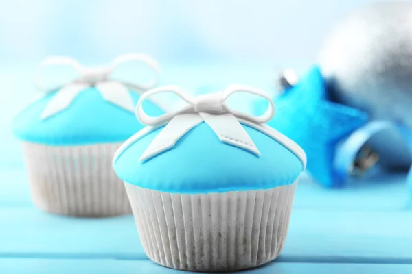 Tasty cupcakes with bow and Christmas toys on color wooden background — Stock Photo, Image