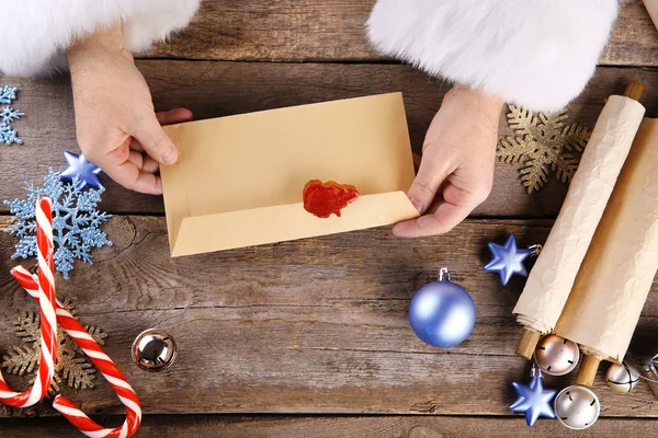 Руки Санта-Клауса с конвертом на деревянном фоне — стоковое фото