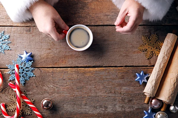Conceito de Natal. Papai Noel toma xícara de café em mãos sobre fundo de madeira, close-up — Fotografia de Stock