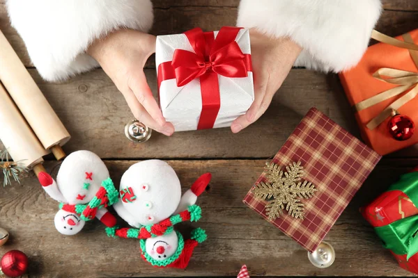 Красивая подарочная коробка в руках Санта-Клауса и рождественские украшения на деревянном столе, крупным планом — стоковое фото