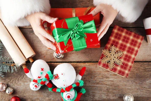 Bella confezione regalo nelle mani di Babbo Natale e decorazioni natalizie su tavolo di legno, primo piano — Foto Stock