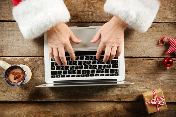 Santa handen typen op laptop op houten tafel, close-up — Stockfoto