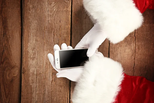Santa Claus's hands with cellphone on wooden background, close up — Stock Photo, Image