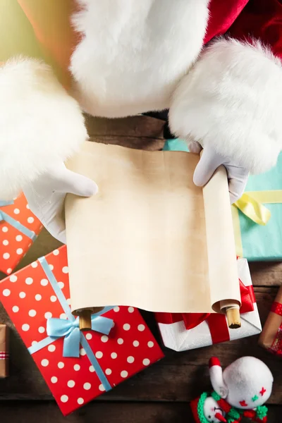 Uma lista de desejos de Natal em mãos de Papai Noel, presentes e brinquedos em fundo de madeira — Fotografia de Stock