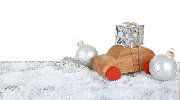 Holzspielzeugauto mit Geschenkbox und Spielzeug auf einem schneebedeckten Tisch vor weißem Hintergrund — Stockfoto