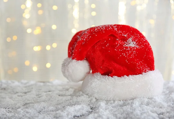 Sombrero de Papá Noel sobre una mesa nevada sobre fondo de brillo —  Fotos de Stock