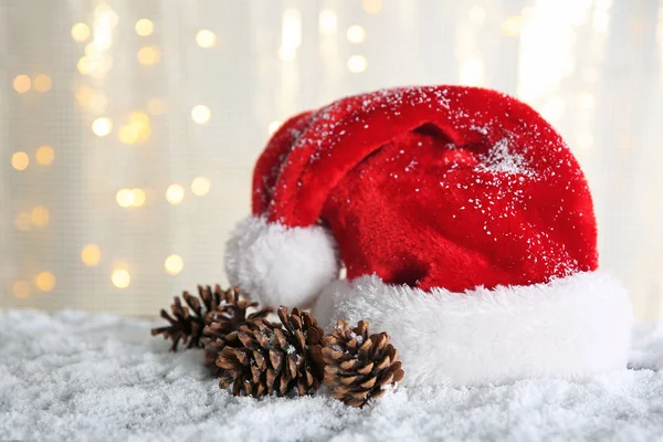 Weihnachtsmann Hut mit Zapfen auf einem schneebedeckten Tisch über Glitzerhintergrund — Stockfoto