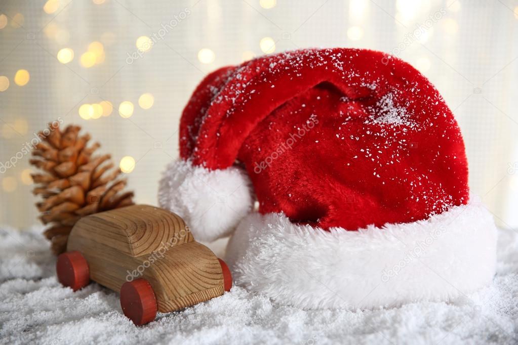 Santa Claus hat with toy car and cone on a snowy table over glitter background