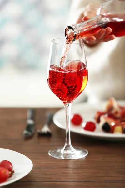 Mladá žena, nalil do sklenice na stole růžové víno — Stock fotografie