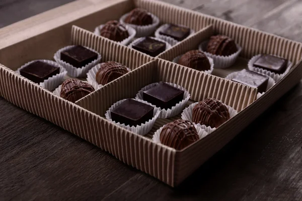 Pyszne cukierki czekoladowe w papier pudełko na drewniane tła, z bliska — Zdjęcie stockowe