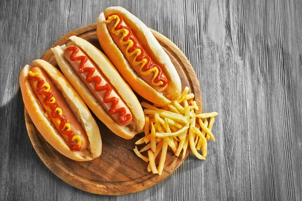 Deliciosos cachorros-quentes com batatas fritas em tábua de corte de madeira, close-up — Fotografia de Stock