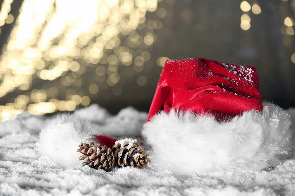 Cappello Babbo Natale rosso con pigne sulla neve artificiale sullo sfondo dorato, primo piano — Foto Stock