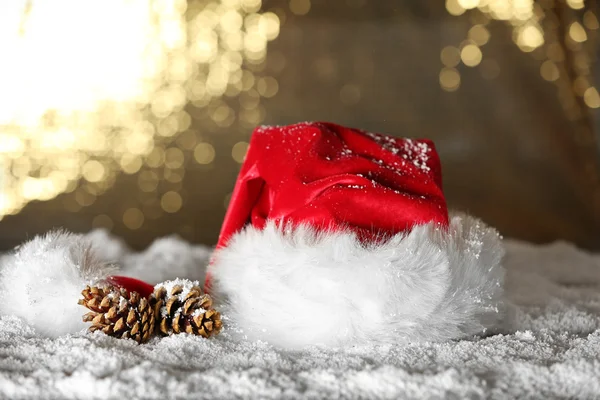 Sombrero rojo de Santa Claus con conos de pino sobre la nieve artificial sobre fondo dorado, de cerca —  Fotos de Stock