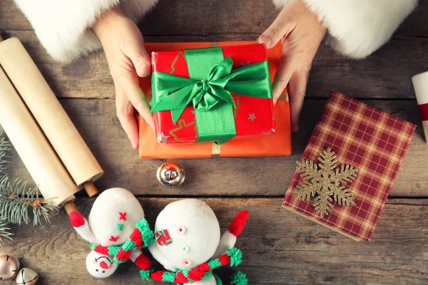 Hermosa caja de regalo en las manos de Santa Claus y decoraciones de Navidad en la mesa de madera, de cerca —  Fotos de Stock