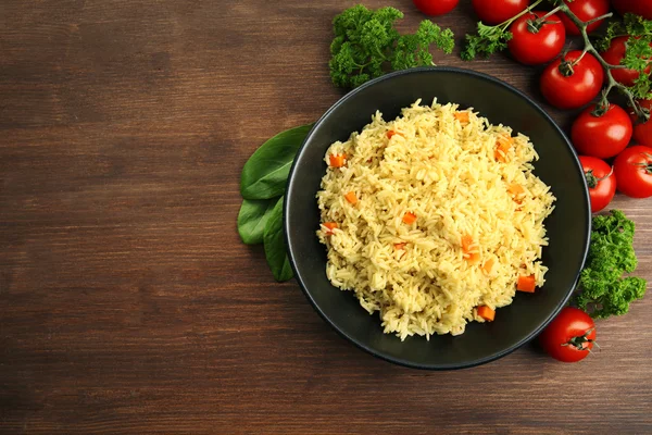 Gedünsteter Reis mit einer Karotte auf einem schwarzen Teller vor Holzhintergrund — Stockfoto