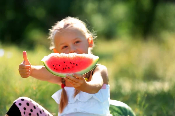 Liten flicka äter vattenmelon på gräsmattan — Stockfoto