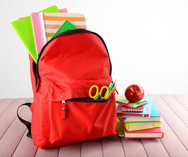 Sabit kırmızı sırt çantası ve yığın beyaz arka plan karşı ahşap masa üstünde tepe üzerinde apple ile kitap dolu