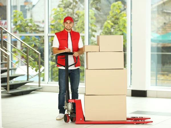 Postbote in roter Uniform mit Paketen auf Dolly — Stockfoto