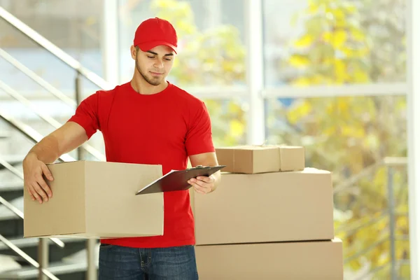 Postman in red uniform holding package — Stock Photo, Image