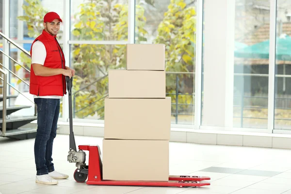 Postbote in roter Uniform mit Paketen auf Dolly — Stockfoto