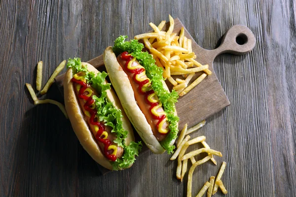 Delicious hot-dogs with French fries on wooden chopping board — Stock Photo, Image