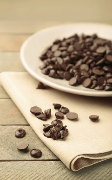 Chocolate morsels on plate, on wooden board — Stock Photo, Image