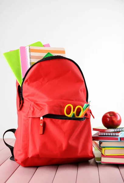 Plein de sac à dos rouge fixe et pile de livres avec pomme sur le dessus sur une table en bois sur fond blanc — Photo