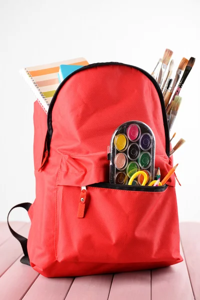 Mochila roja llena de papelería sobre mesa de madera sobre fondo blanco — Foto de Stock