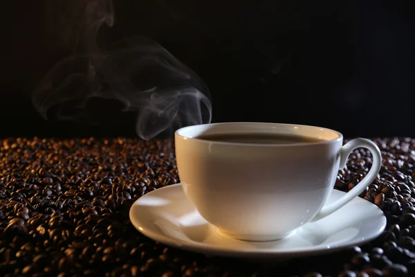 Kop warme koffie onder koffie bonen op donkere achtergrond — Stockfoto